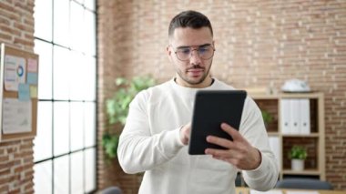 Young hispanic man business worker smiling confident using touchpad at office