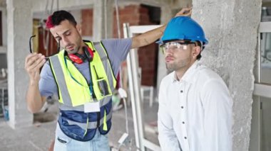 İnşaat alanında iki erkek müteahhit ve mimar stresli bir ifadeyle bir arada duruyorlar.