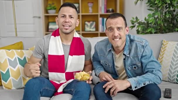 Два Чоловіки Підтримують Футбольну Команду Сидять Дивані Вдома — стокове відео