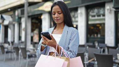 Afro-Amerikalı bir kadın kahve dükkanının terasında akıllı telefon kullanıyor.