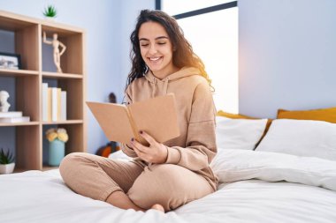 Yatak odasında kitap okuyan genç İspanyol kadın.