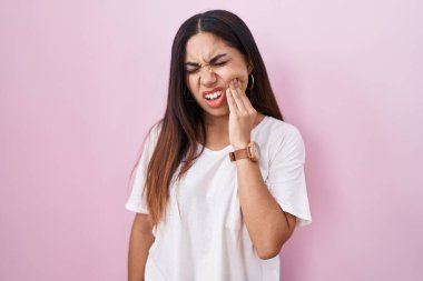 Pembe arka planda duran genç bir Arap kadın diş ağrısı ya da diş hastalığından dolayı acı dolu bir ifadeyle ağıza dokunuyor. dişçi 