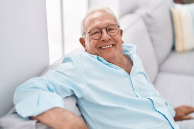 Senior grey-haired man smiling confident sitting on sofa at home