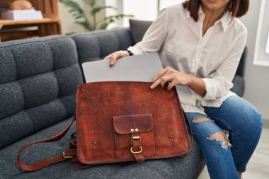 Young beautiful hispanic woman business worker holding laptop of briefcase at office