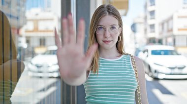 Young blonde woman doing stop gesture with hand at street