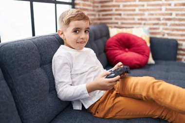Adorable hispanic boy playing video game sitting on sofa at home