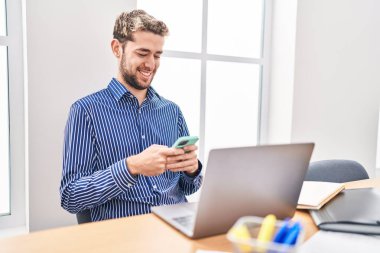 Ofiste dizüstü bilgisayar ve akıllı telefon kullanan genç bir iş adamı.