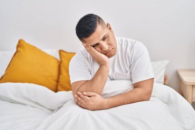 Young latin man stressed sitting on bed at bedroom
