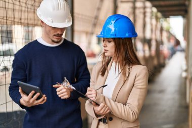 Mand and woman architects using touchpad write on report at street