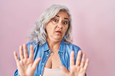 Pembe arka planda gri saçlı orta yaşlı bir kadın. Avuçlarını hareket ettiriyor. Korkmuş ve iğrenç bir ifadeyle reddediyor. Dur ve yasakla. 