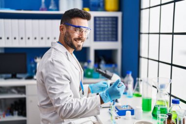 Laboratuvarda sıvı ölçen bilim adamı üniforması giyen İspanyol genç adam.