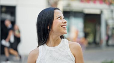 Young beautiful hispanic woman smiling confident looking to the sky at street