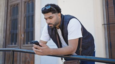 Afro-Amerikalı adam akıllı telefon kullanıyor ve sokakta ciddi bir ifade kullanıyor.