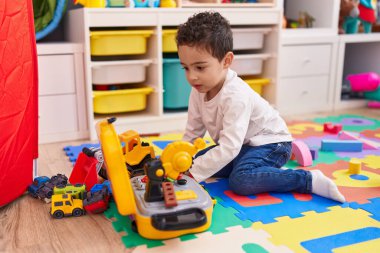 Anaokulunda yerde oturan sevimli İspanyol çocuk araba oyuncağıyla oynuyor.