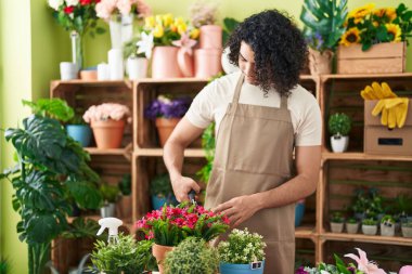 Young latin man florist cutting plants at flower shop