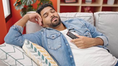 Uzaktan kumandalı Afro-Amerikan adam kanepede uzanıyor ve evde uyuyor.