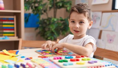 Anaokulunda masada oturmuş matematik oyunu oynayan sevimli beyaz çocuk.
