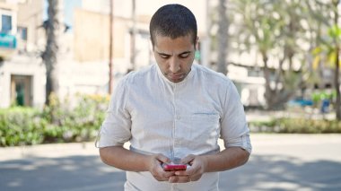 Young hispanic man using smartphone at park