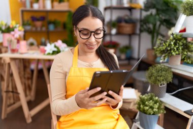 Young arab woman florist smiling confident using touchpad at flower shop