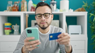 İspanyol adam yemek odasında akıllı telefonuyla online alışveriş yapıyor.