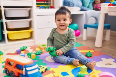 Anaokulunda yerde oturan sevimli İspanyol çocuk timsah oyuncağıyla oynuyor.