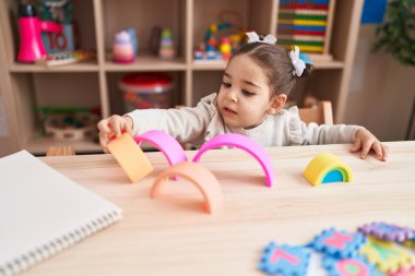 Anaokulundaki masada oturan, inşaat bloklarıyla oynayan sevimli İspanyol kız.