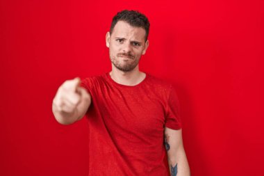 Kırmızı arka planda dikilen İspanyol genç adam kameraya kızgın ve sinirli olduğunu gösteriyor. 