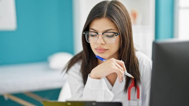 Genç beyaz kadın doktor klinikte bilgisayar okuyarak tıbbi rapor veriyor.