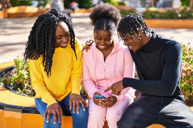 Parkta bankta oturan Afrikalı Amerikalı arkadaşlar akıllı telefon kullanıyorlar.