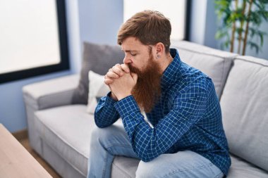 Young redhead man stressed sitting on sofa at home