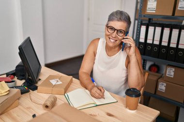 Middle age woman ecommerce business worker talking on the smartphone at office