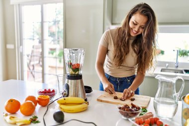 Genç ve güzel İspanyol kadın mutfakta sebze suyu ve blender karışımı hazırlıyor.