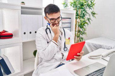 Klinikteki masada oturan dokunmatik ped kullanan genç İspanyol doktor.