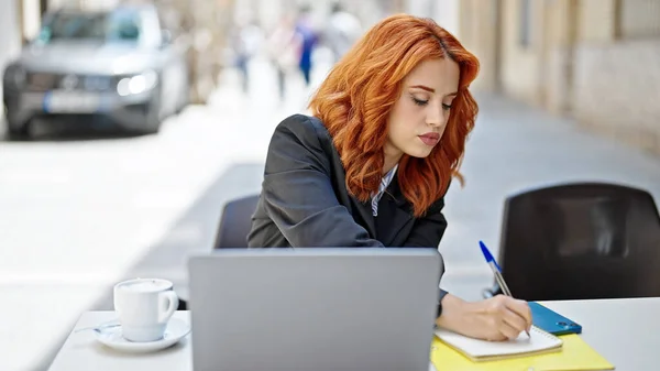 若い赤毛の女性のビジネスワーカーは コーヒーショップテラスでノートを取るラップトップを使用して — ストック写真