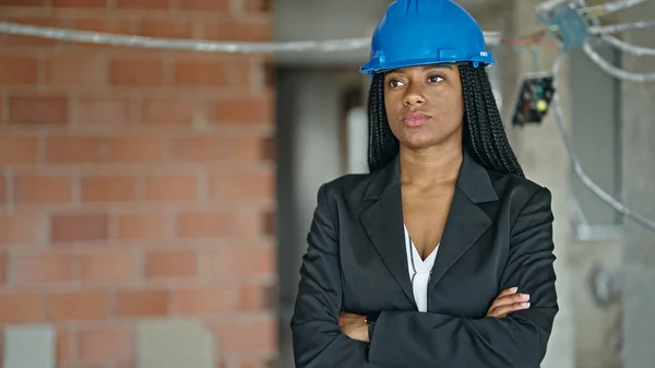 アフリカ系アメリカ人の女性建築家が腕を組んで立ち上がり 建設現場で真剣な表情を見せる — ストック写真