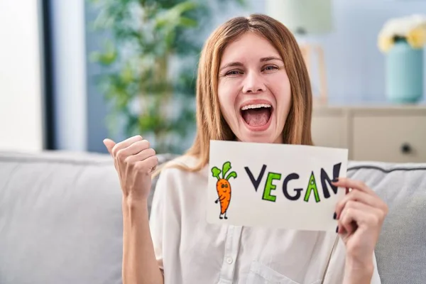 stock image Beautiful woman holding banner with vegan word pointing thumb up to the side smiling happy with open mouth 