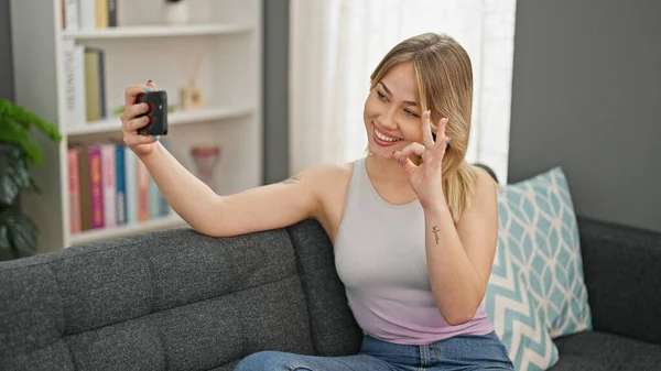 stock image Young blonde woman taking selfie picture with smartphone sitting on the sofa at home