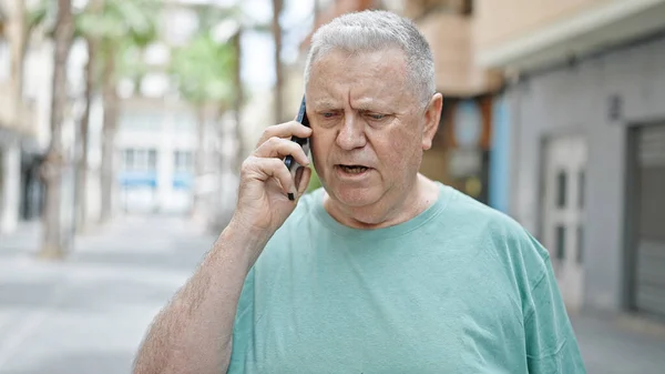 ストリートで真剣な表情でスマートフォンで話す中年白髪の男 — ストック写真