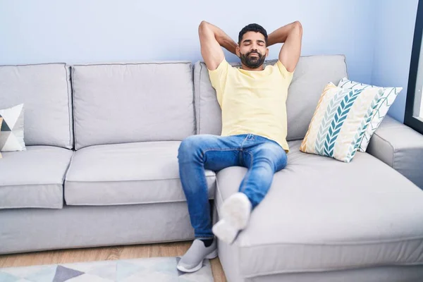 年轻的阿拉伯男子放松了下来 双手放在头上 坐在家里的沙发上 — 图库照片