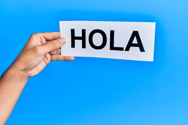 stock image Hand of caucasian man holding paper with hola word over isolated blue background
