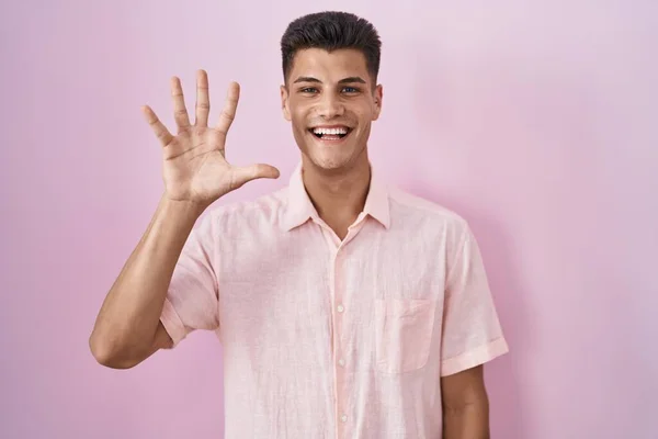 年轻的惊慌失措的男人站在粉色的背景上 露出五号手指指尖 面带微笑 自信而快乐 — 图库照片