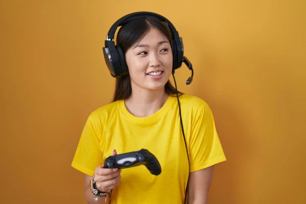 中国年轻女子玩电子游戏时牵着控制器 面带微笑地望向一边 自然的表情 充满自信地大笑 — 图库照片