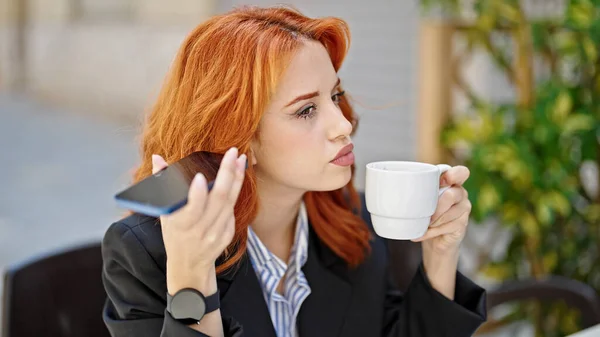 若い赤毛の女性ビジネスワーカーコーヒーショップのテラスでコーヒーを飲むスマートフォンによる音声メッセージを聞く — ストック写真