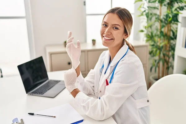 stock image Young hispanic woman wearing doctor uniform wearing gloves at clinic