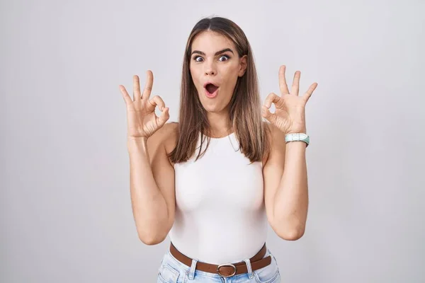站在白人背景上的西班牙裔年轻女性惊讶地 震惊地用手指做着一个认可的符号 疯狂的表达 — 图库照片