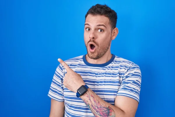 Young Hispanic Man Standing Blue Background Surprised Pointing Finger Side — Stock fotografie