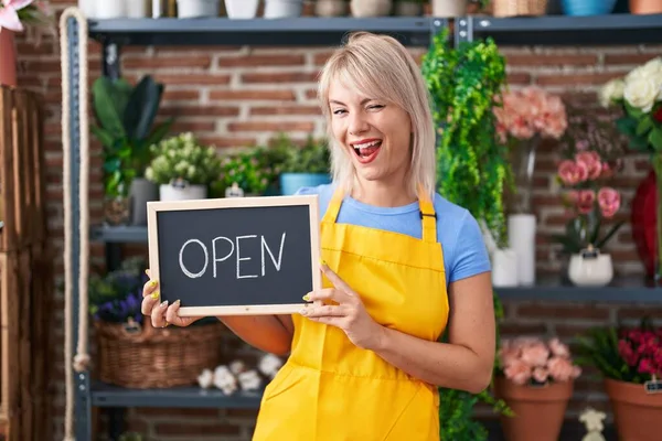 Young caucasian woman working at florist holding open sign winking looking at the camera with sexy expression, cheerful and happy face.