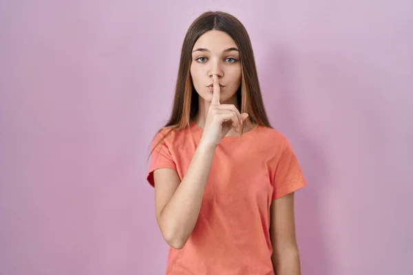 10代の少女ピンクの背景の上に唇に指で静かにするように求めて立っている 沈黙と秘密の概念 — ストック写真