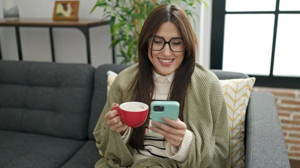 Young Beautiful Hispanic Woman Using Smartphone Drinking Coffee Home — Stockfoto