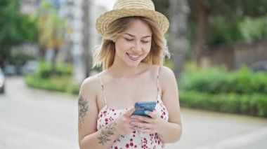 Young blonde woman tourist smiling confident using smartphone at street